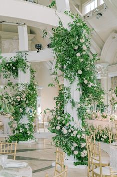 an indoor wedding venue with white flowers and greenery on the columns, gold chairs and tables