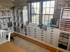 a room filled with lots of white drawers and shelves next to a table in front of a window