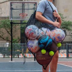 a man holding a bag full of balls on top of a basketball court in front of a building