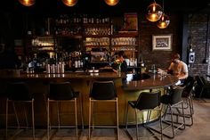 a man sitting at a bar with lots of bottles on the shelves and chairs in front of him