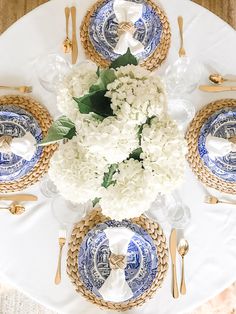 the table is set with blue and white plates, silverware, and hydrangeas