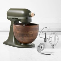 an olive green stand mixer with wooden bowl next to it's attachments and other kitchen accessories