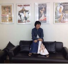 a woman sitting on top of a black couch in front of three framed posters above her