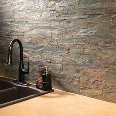 a kitchen sink sitting under a faucet next to a stone wall