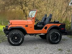 an orange jeep with black leather seats parked in gravel area next to trees and bushes