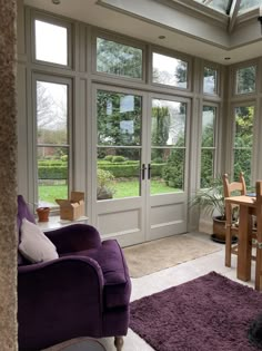 a living room filled with purple furniture and lots of glass doors leading to a garden