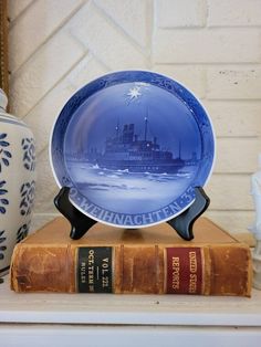 a blue plate sitting on top of a book next to a vase and two books