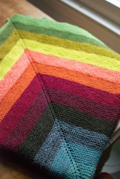 a multicolored knitted dishcloth sitting on top of a wooden table next to a window