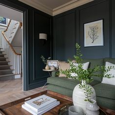 a living room with dark green walls and wooden flooring, white vases on the coffee table