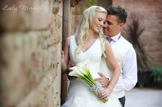 a bride and groom standing next to each other in front of a brick wall holding flowers