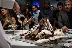 a group of people standing around a table filled with desserts and wineglasses