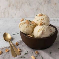 two scoops of ice cream in a bowl with nuts on the table next to it