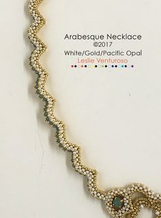 an elaborate necklace is displayed on a white surface with gold and green beads in the shape of a heart