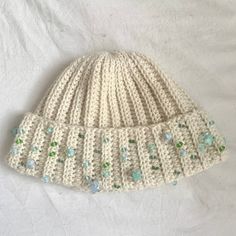 a white knitted hat with green and blue beads on it's brim