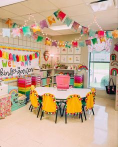 a classroom filled with lots of tables and colorful decorations on the wall above them is a white table topped with yellow chairs