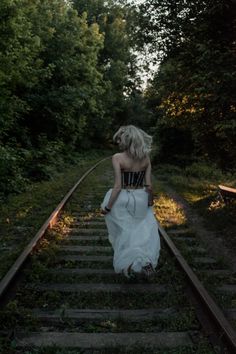 a woman is walking down the railroad tracks in a white dress and black bra top