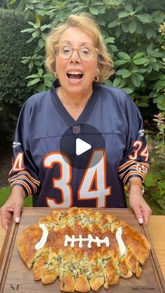 a woman holding a tray with a pizza on it and an american football jersey in the background