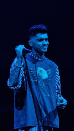 a man holding a microphone up to his ear while standing in front of a dark background