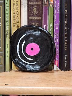 a book shelf with books and a black painted disk on top of it, sitting in front of a row of other books