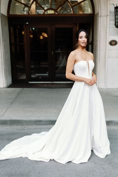 a woman standing in front of a building wearing a white wedding dress and posing for the camera