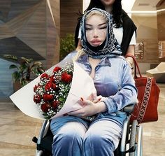 a woman sitting in a wheel chair with flowers on her lap and another woman standing behind her