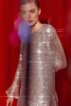 a woman standing in front of a red background wearing a silver dress with sequins on it