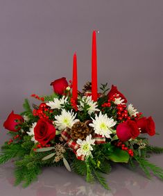 a christmas centerpiece with red roses and white daisies, pine cones and candles