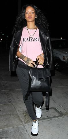 a woman in pink shirt and black pants walking down the street with her handbag