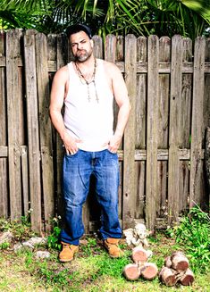 a man standing in front of a fence with his hands on his hips and wearing jeans