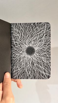 a hand is holding an open book with black and white designs on the front cover