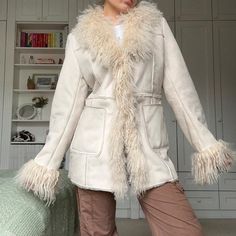 Plush Shearling Coat with Shaggy Fur Trim in Beige Embrace timeless elegance and exceptional warmth with this plush shearling coat featuring luxurious shaggy fur trim. Designed to offer the ultimate blend of comfort and style, this coat is perfect for cold-weather fashionistas seeking to elevate their wardrobe. Whether you're strolling through the city, heading to a dinner party, or bundling up for a chilly day, this coat is the epitome of cozy sophistication. Premium Materials & Craftsmanship This coat is meticulously crafted from high-quality shearling, giving it a soft, velvety texture that feels both comfortable and warm. The coat's standout feature is its bold, shaggy fur trim, which runs along the wide collar, down the front edges, and around the cuffs, providing a statement-making c Afghan Coat, Mongolian Fur, Penny Lane Coat, Trend Forecast, Coat White, Boho Jacket, Sheepskin Coat, Classic Wardrobe Staples, Coat Winter