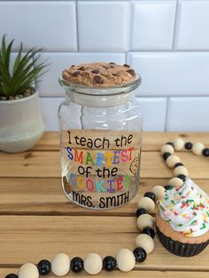 a cookie in a jar next to some beads on a table with a cupcake