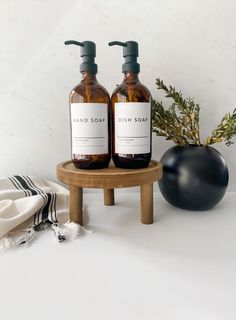 two bottles of hand soap sitting on a table next to a potted plant and towel