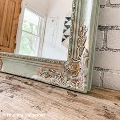 a mirror sitting on top of a wooden table next to a brick wall and window