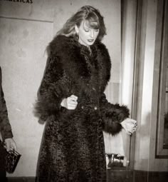 black and white photograph of woman in fur coat walking down the street with handbag