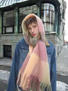 a young man wearing a scarf and jacket in front of a building