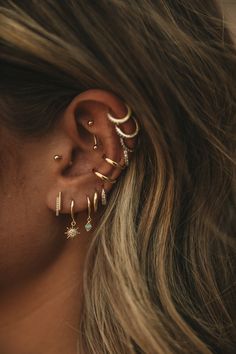 a woman wearing ear piercings with stars and moon designs on her ears, looking down at the ground