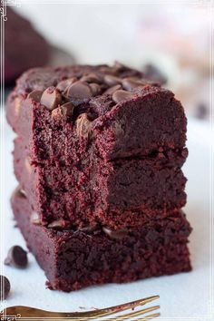 three chocolate brownies stacked on top of each other next to a fork and knife