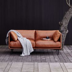 a brown leather couch sitting next to a tree