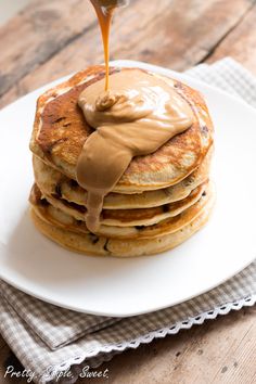 a stack of pancakes with syrup being drizzled over them on a white plate