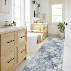 a bath room with a tub a sink and a rug on the floor in front of a window