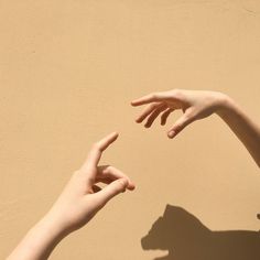 two hands reaching towards each other in front of a beige wall with shadows on it