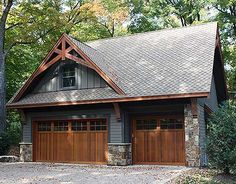 a two car garage with stone and wood accents on the roof, surrounded by trees