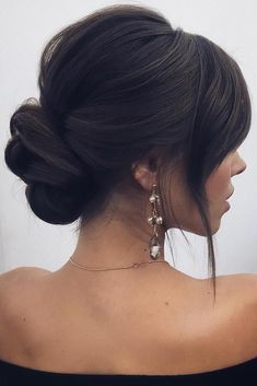 a woman with her hair in a low bun, wearing earrings and a black dress