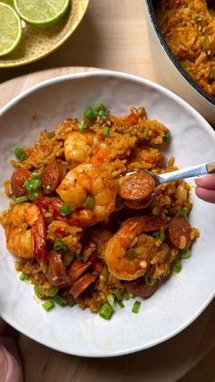 a person holding a spoon over a plate of food with shrimp and rice on it