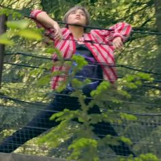 a woman standing on top of a wooden bridge in the middle of a forest with her arms stretched out