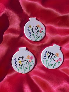 two personalized ceramic ornaments sitting on a pink satin surface with the word mom painted on them