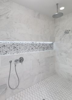 a bathroom with white marble walls and flooring, shower head and hand held faucet