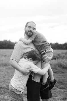 a man is holding two boys on his shoulders in the middle of an open field