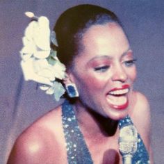 a woman with a flower in her hair holding a microphone and singing into the microphone